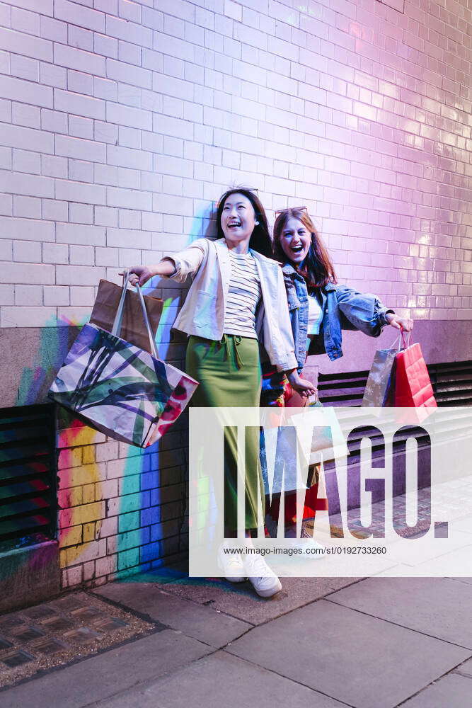 Cheerful Lesbian Couple With Shopping Bags By Brick Wall Model Released