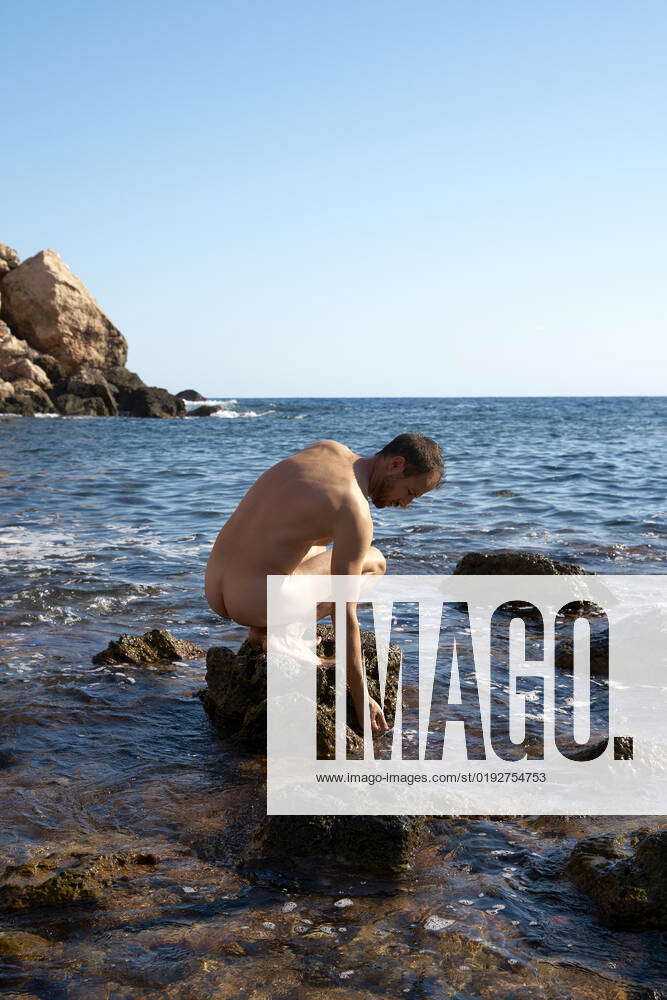 Naked man sitting on rock amidst sea at sunny day model released, Symbolfoto