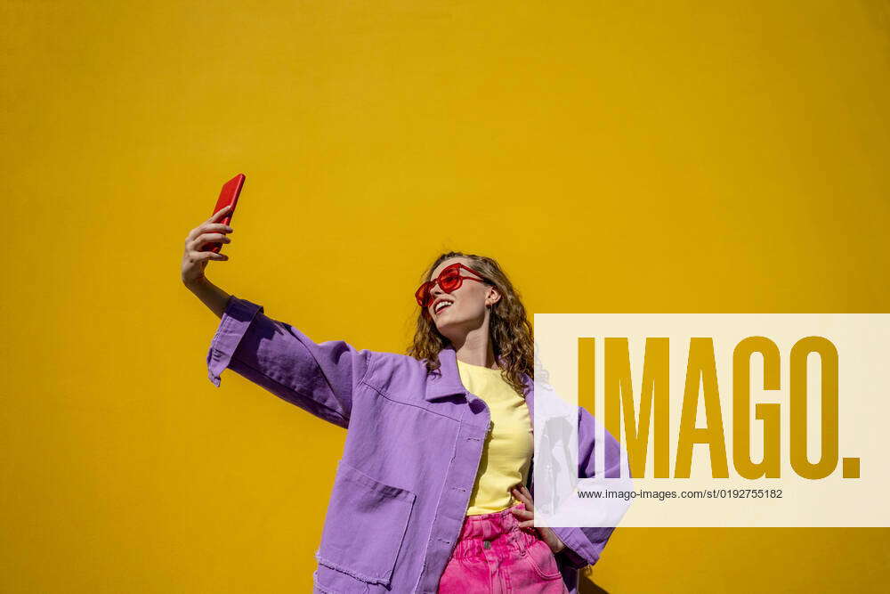 Woman with hand on hip taking selfie through mobile phone in front of