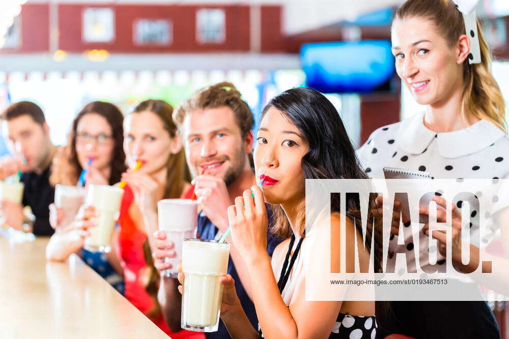 Friends Or Couples Eating Fast Food And Drinking Milk Shakes On Bar In American Fast Food Diner