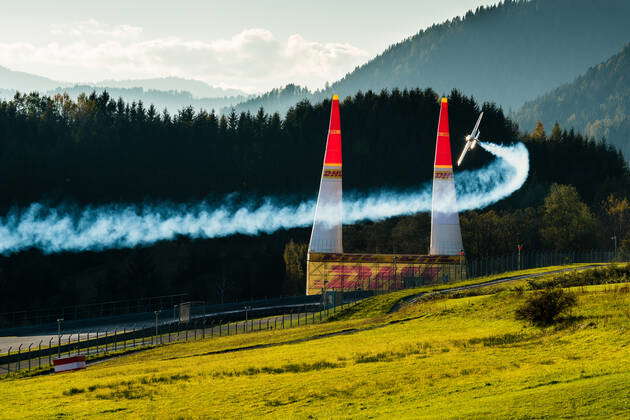 A stunt flying aeroplane, releasing smoke, is flying through 2 pylons ...