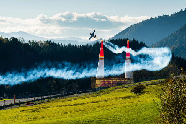 A stunt flying aeroplane, releasing smoke, is flying through 2 pylons ...