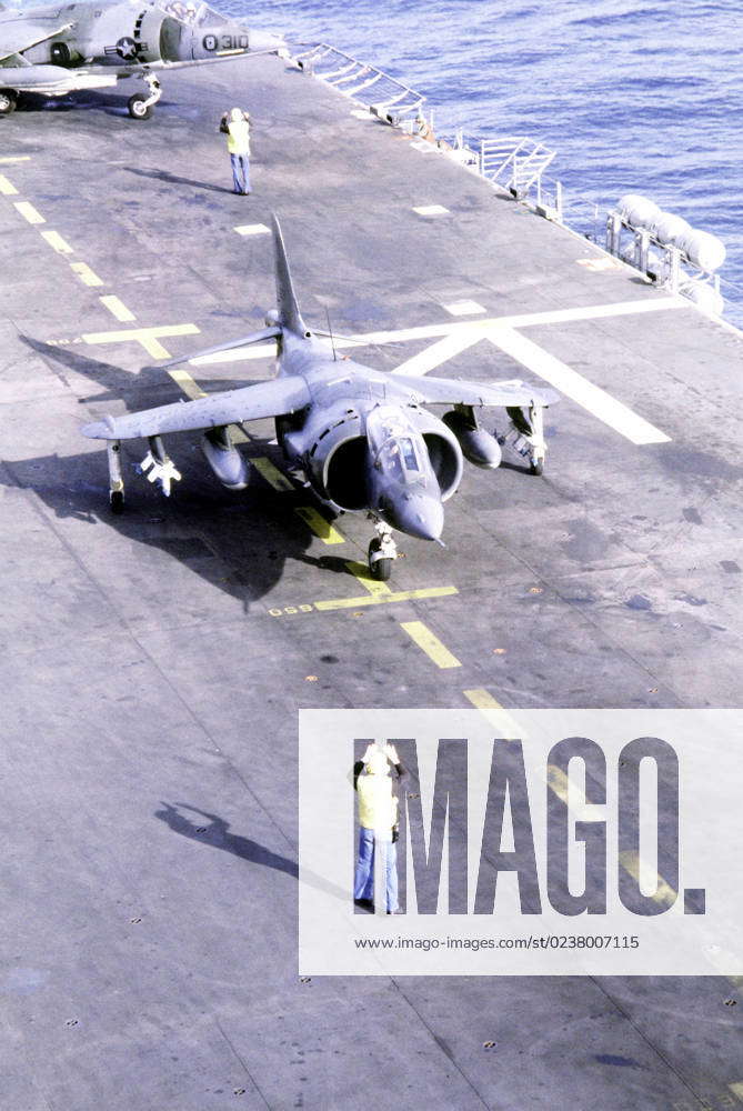 A flight deck crewman signals to the pilot of an AV-8A Harrier aircraft ...