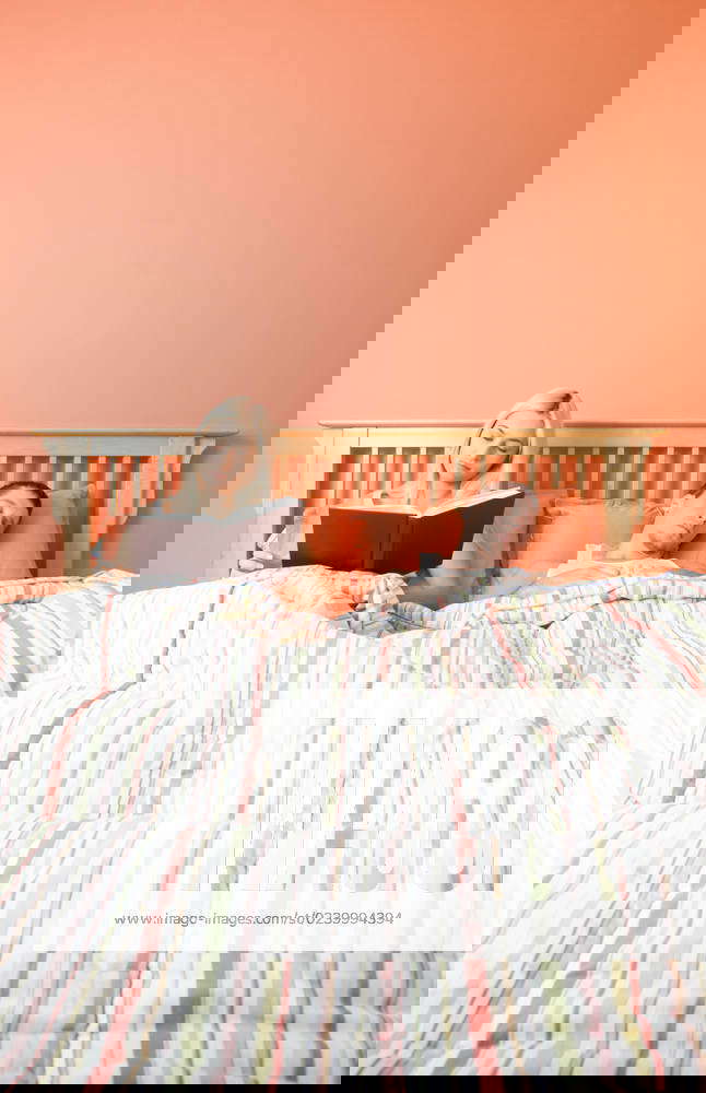 View of couple in bed, with woman reading book and man sleeping