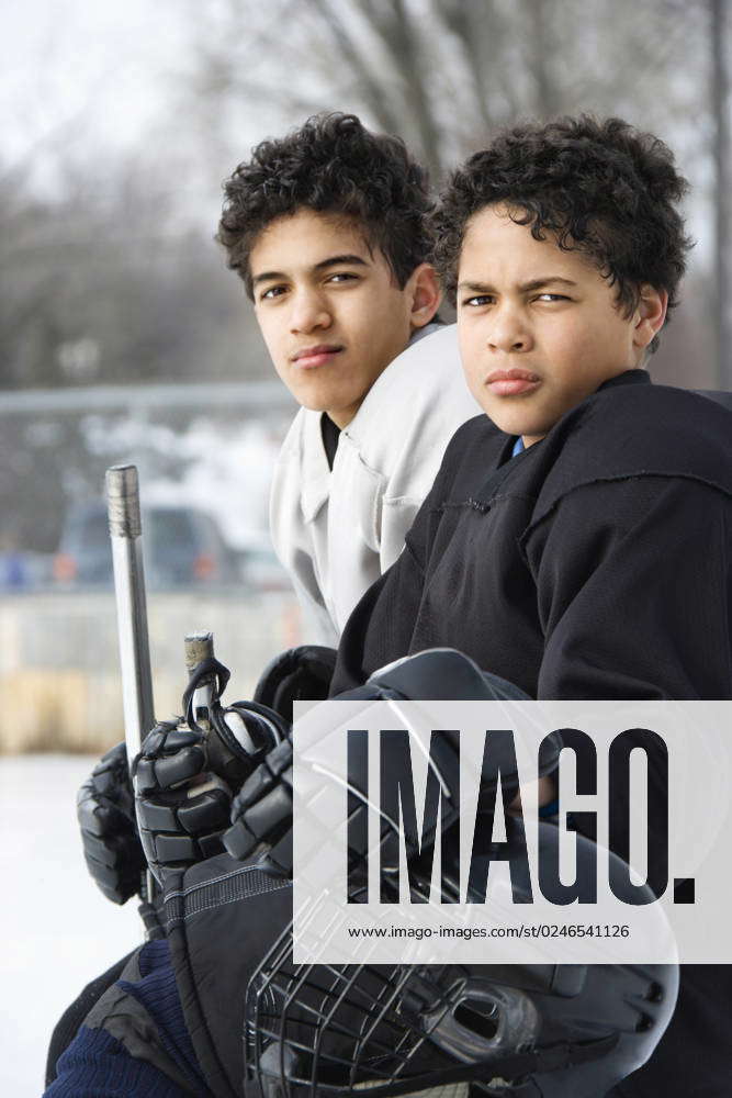 Two boys in ice hockey uniforms sitting on ice rink sidelines