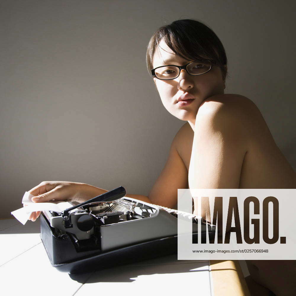 Pretty nude young Asian woman sitting at kitchen table with typewriter