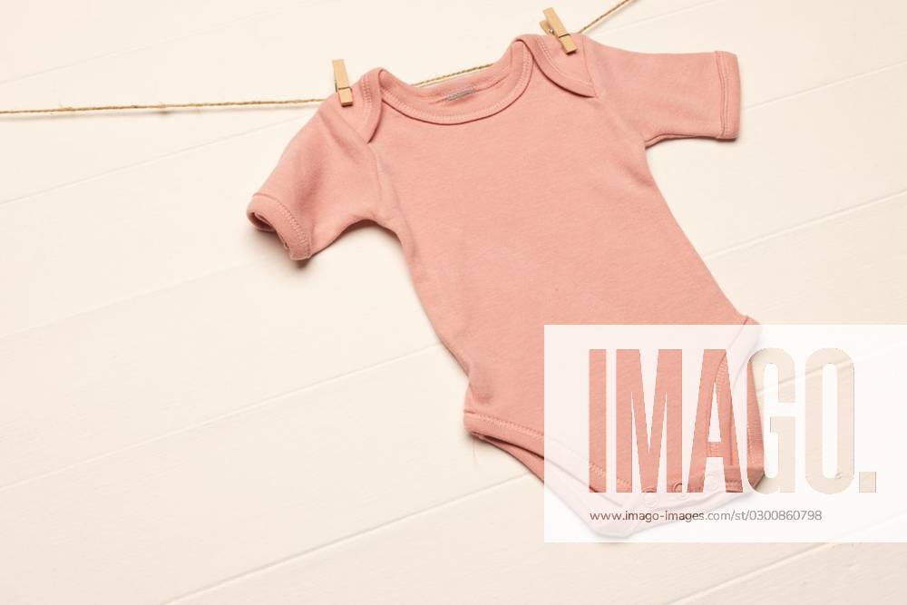 Pink baby grow hanging with clothes pegs with copy space on white ...