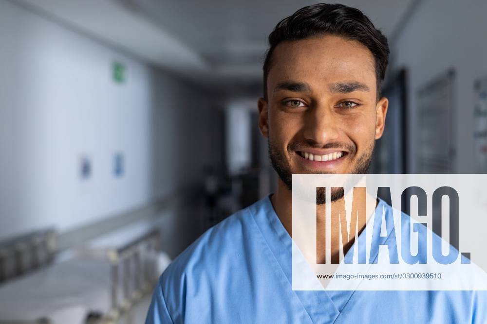 Portrait of happy biracial male doctor wearing scrubs in corridor at ...