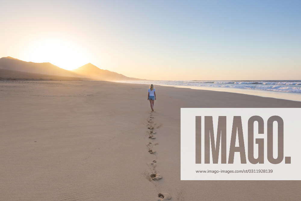 Woman walking on sandy beach in sunset leaving footprints in the sand ...