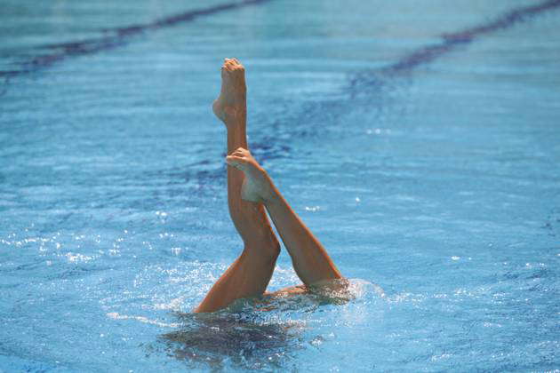 Synchronized swimmers legs point up out of the water in action 