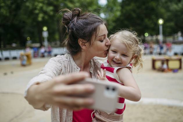 Little toddler girl and mother having fun at playground taking selfies ...