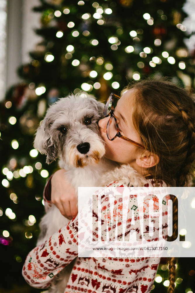 Tween girl with blond hair and glasses gives kiss to schnoodle pup