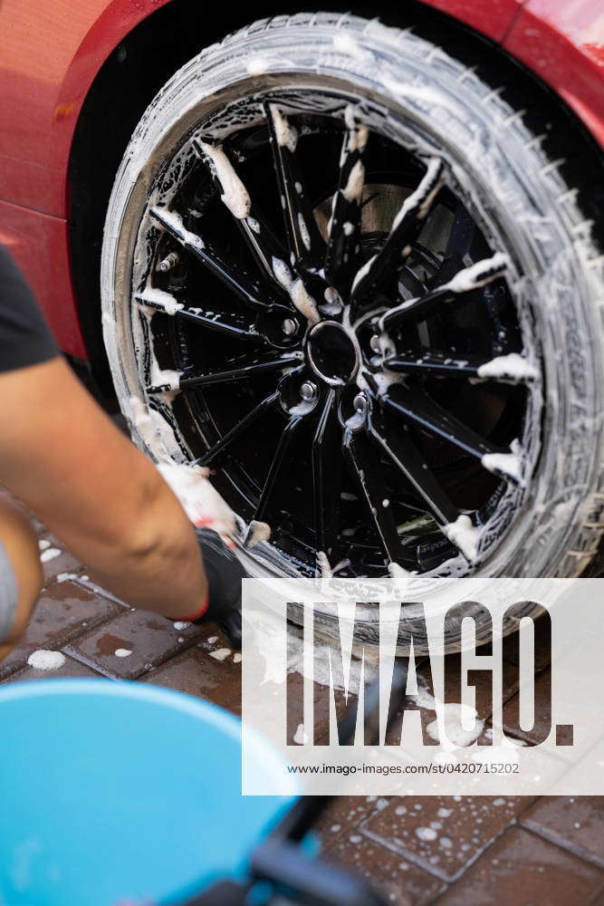 A person manually scrubs a car tire with foamy detergent, detailing the ...