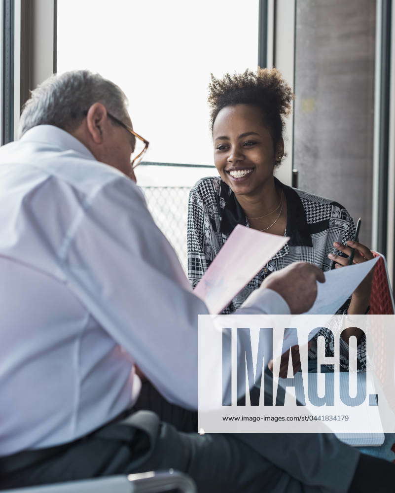 Smiling businesswoman with senior colleague discussing over document at  office model released