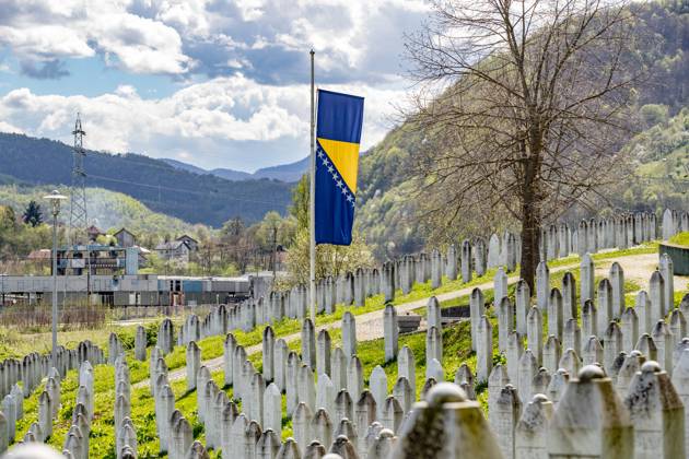 A Bosnian flag stands at half-mast, facing a wave of graves at the ...