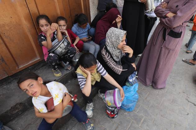 Men, women, and children queue to receive food rations from a public ...