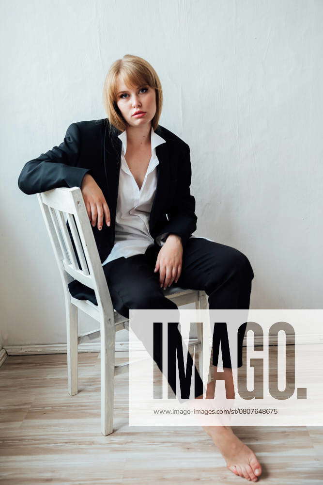 Beautiful fashionable woman in black business suit sitting on a chair ...