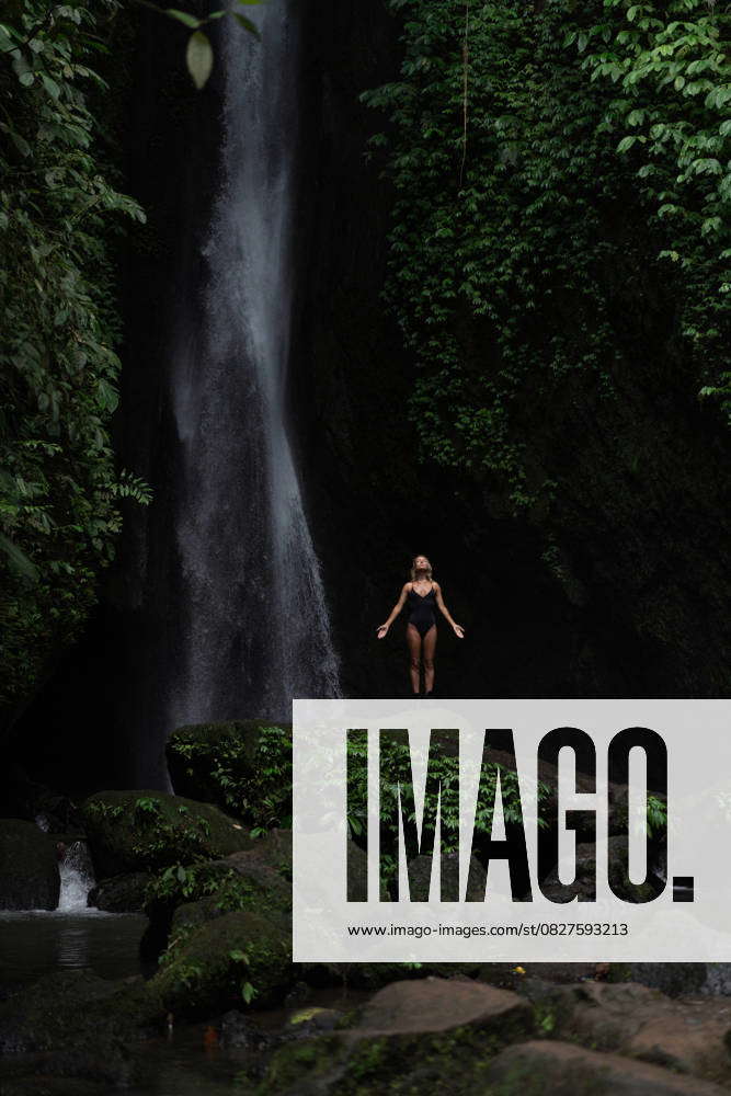 Woman meditating under powerful tropical waterfall in green jungle Ubud ...